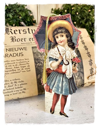 Een mooi gestanst in reliëf victoriaans ornament van meisje met paraplu wat ook kan staan. Afm. 19 cm. groot x 8 cm. breed
