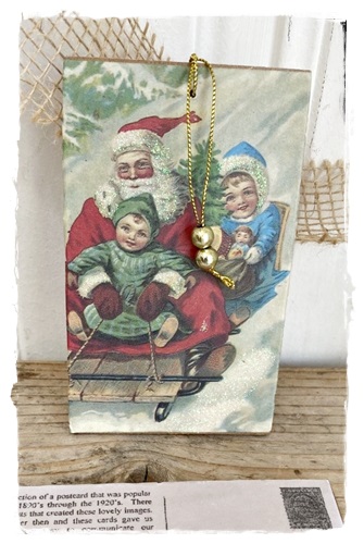 Postcard van hout aan goudkleurig koordje 13 x 8 cm. met victoriaanse afb. Sleeen met Santa glittertjes